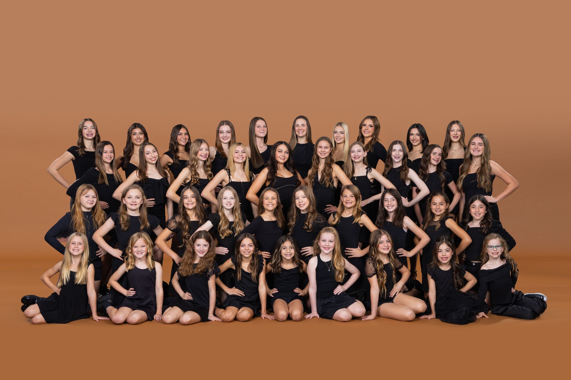 Studio Z dancers posing together in black on a warm tan backdrop